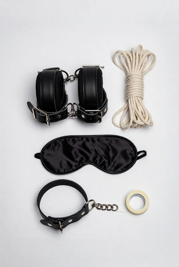 Black faux leather cuffs, blindfold, collar and white rope arranged as a beginner bondage kit