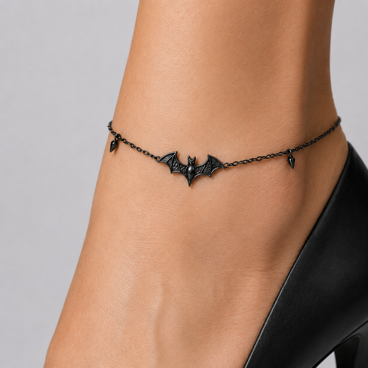 Bat charm gothic anklet - black bat pendant with spike side charms on a fine chain, close-up on the ankle