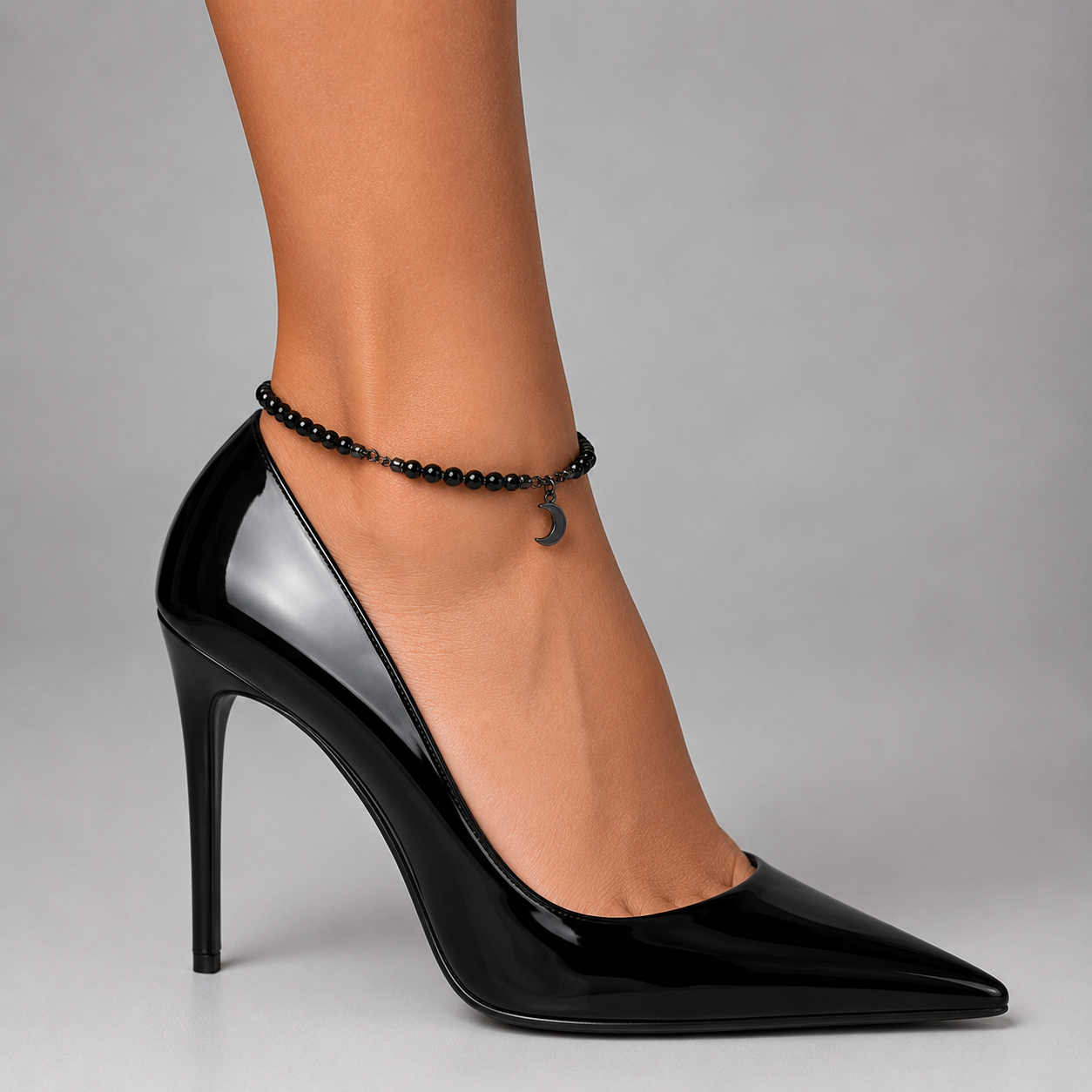 Black beaded ankle bracelet with onyx-look beads and moon charm on an ankle - side view with black heels
