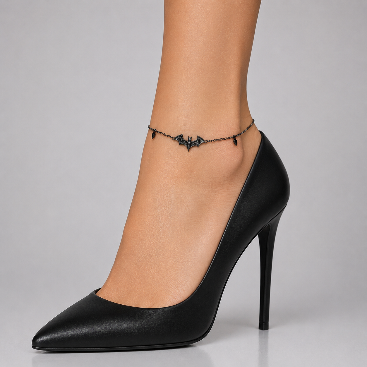 Gothic bat ankle bracelet with mini spike details on a gunmetal chain - angled view with black heels